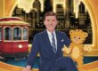A rich, nostalgic illustration of Fred Rogers sitting on his set, red trolley by his side, Daniel Tiger puppet in hand, with the Pittsburgh skyline glowing in the window behind him. Warm golden tones evoke kindness, familiarity, and timeless wisdom.