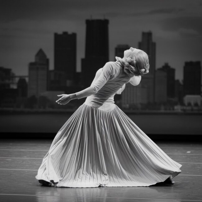 A dramatic, vintage illustration of Martha Graham performing “Lamentation” in her iconic stretch fabric costume, with Pittsburgh’s skyline subtly reflected in the background — capturing both movement and emotional intensity.