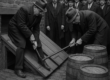 Black-and-white 1920s scene of Prohibition agents prying open a cellar door during a raid on an illegal Pittsburgh speakeasy, with barrels of liquor and onlookers visible.
