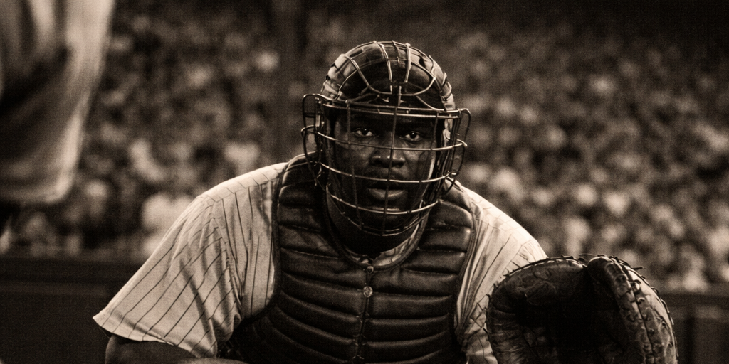 baseball-player Baseball catcher in 1940s uniform crouches behind home plate at a packed Pittsburgh stadium, capturing the era when Josh Gibson was considered the greatest hitter in baseball.