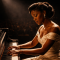 A Black female jazz pianist performs under a single spotlight on a concert stage, hands on the keys of a grand piano, capturing the mastery and artistic authority of Mary Lou Williams at the height of her career.
